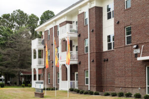 Exterior of a brick apartment building with two flags on flag poles outside.